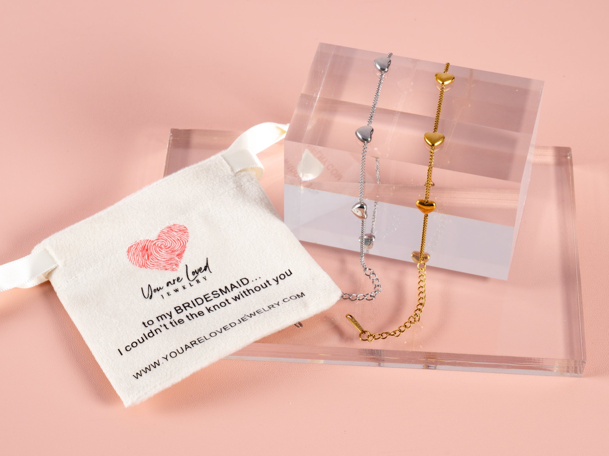 multi heart gift bracelets shown here on a clear cube and a pink bridesmaid can't tie the knot without you gift pouch next to it. These are great gift bracelets for all your bridesmaids