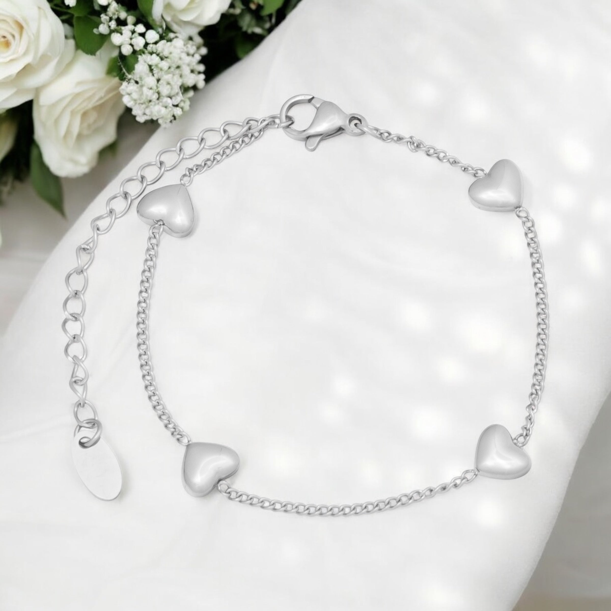 Silver heart-shaped bracelet on a white surface with flowers in the background