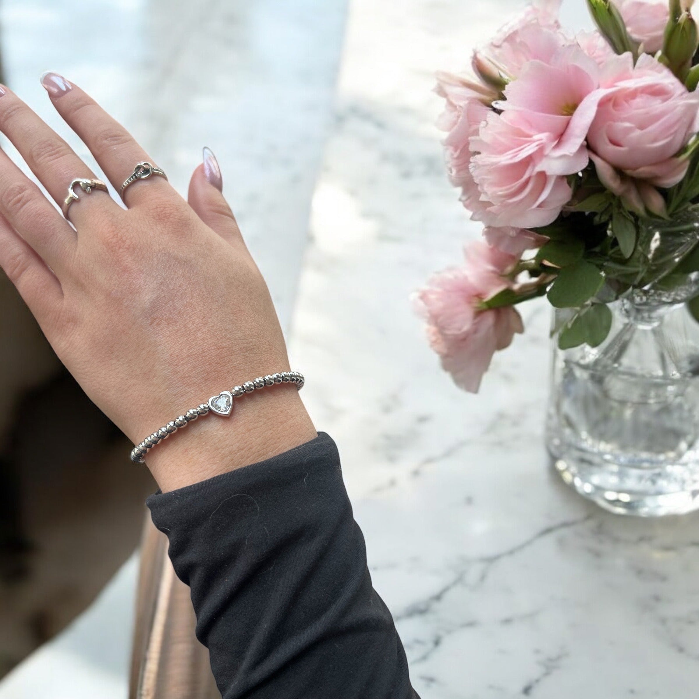 a silver gemstone heart bracelet that is shown on  a wrist with flowers. This gemstone silver heart bracelet is adjustable and can be given as a bridesmaid gift jewelry
